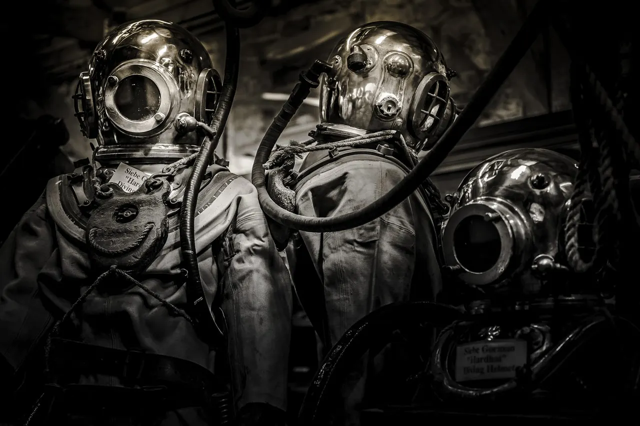 Vintage diving suits with large metal helmets and air hoses displayed in a museum setting.