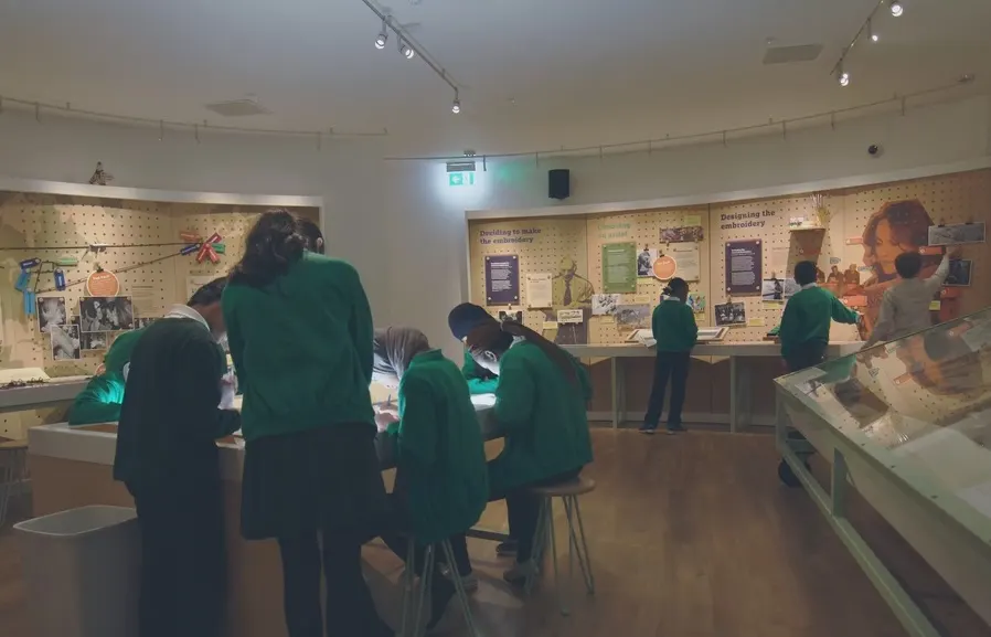 School group in green uniforms exploring a museum exhibition space with displays and interactive panels.