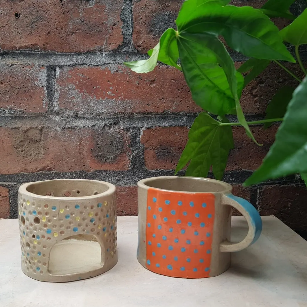 Two handmade ceramic vessels with coloured polka dot patterns displayed against a brick wall with climbing ivy.