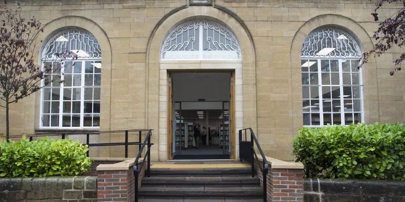 Stone building facade with arched windows, entrance doorway, and steps leading to library entrance.
