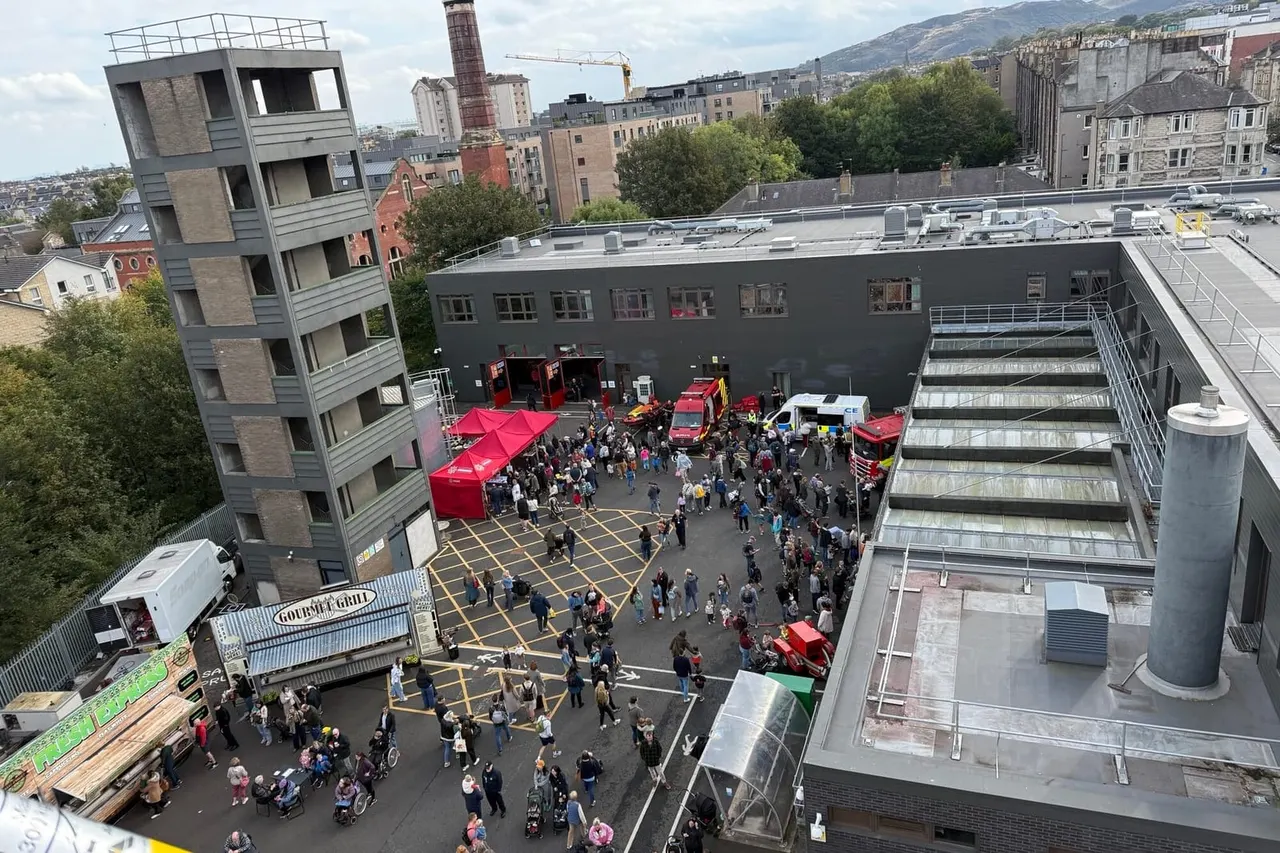 Overhead view of a crowd gathered in a courtyard with fire engines and red marquees during an outdoor event.