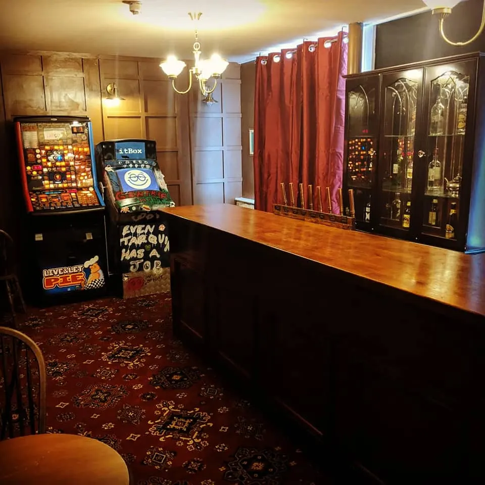An escape room interior with arcade machines, a wooden counter, red curtains, and glass display cabinets under warm lighting.
