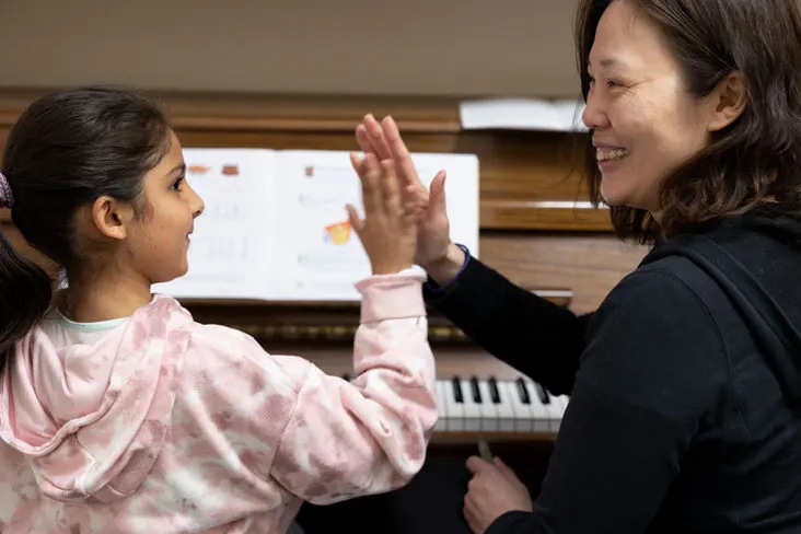 An adult instructor and young student high-five during a piano lesson.
