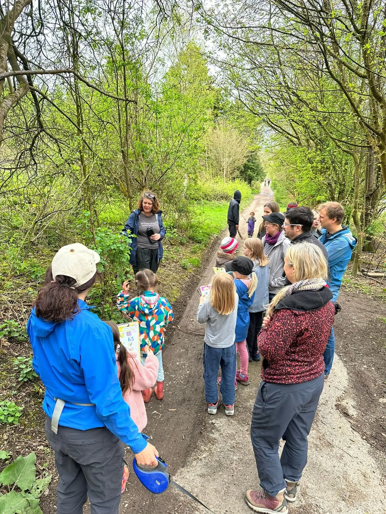 A group of adults and children on a guided woodland walk along a tree-lined path in spring.