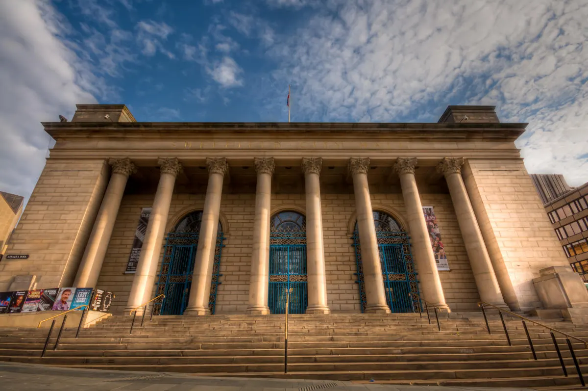 Classical stone building with tall Corinthian columns, blue doors and blue sky above.
