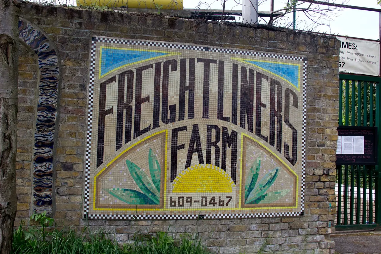 Mosaic sign for Freightliners City Farm mounted on a brick wall with a sun and leaf design.