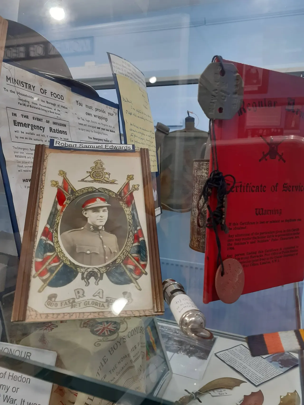 Museum display case containing First World War memorabilia including framed portrait, emergency rations tin, certificate and historical documents.