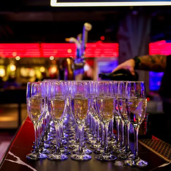 Row of champagne flutes filled with sparkling wine on a bar counter in a nightclub with neon lighting.