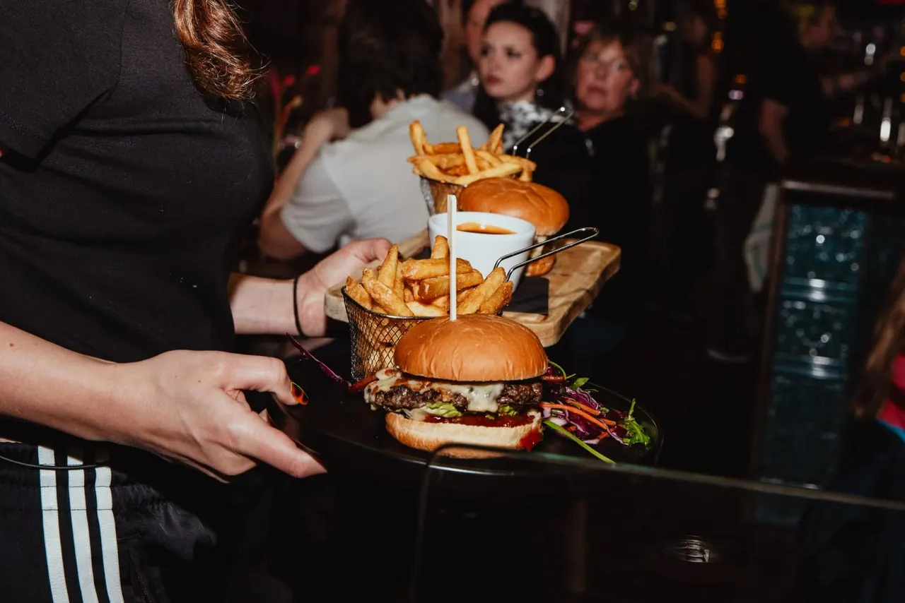 Staff member serving burgers and chips to guests at a busy indoor event.