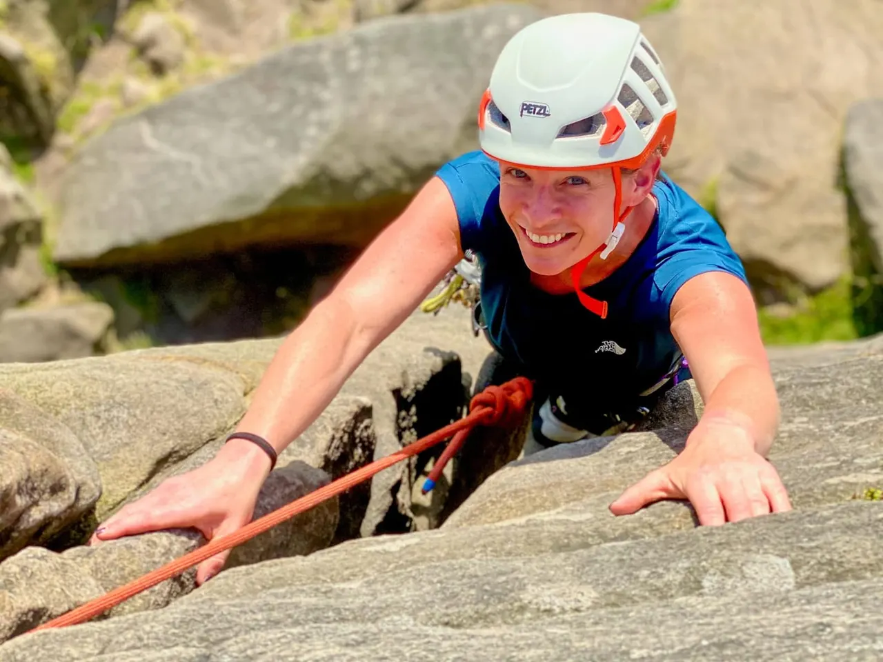 Young person rock climbing outdoors on a rocky cliff face with safety helmet and rope.
