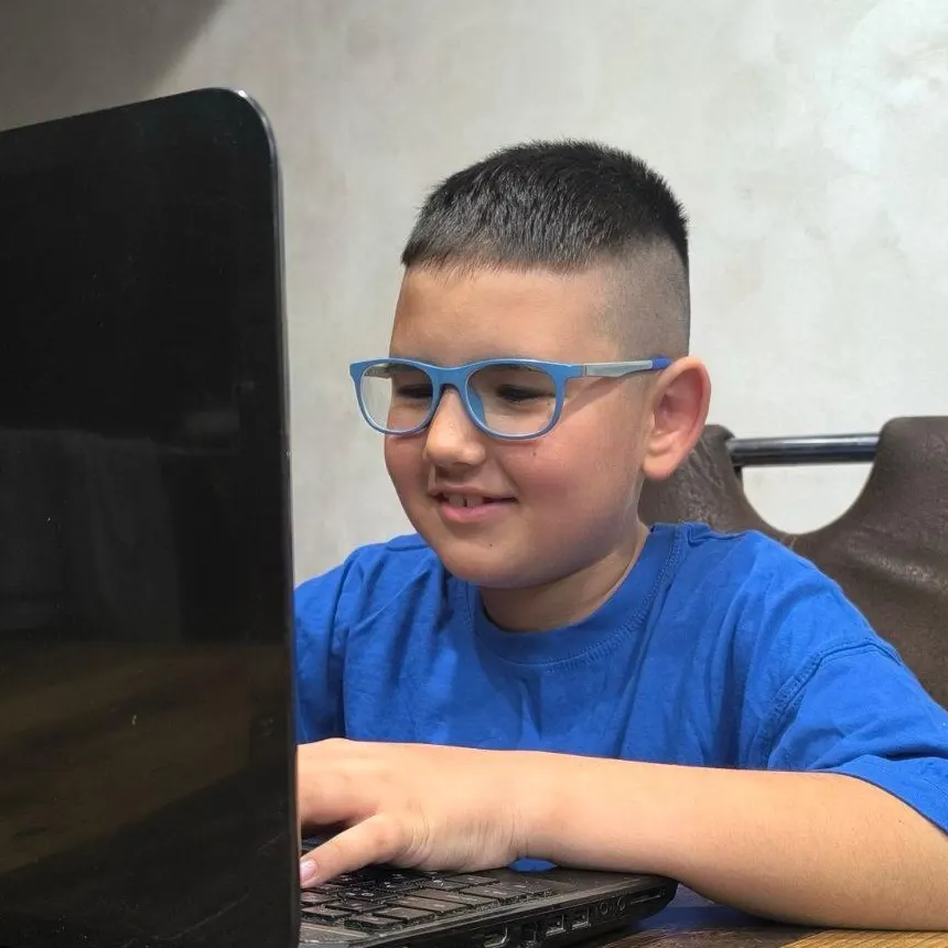 Child in blue shirt and glasses using a laptop for a coding session.