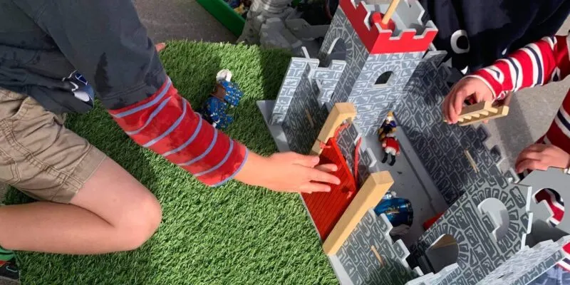 Children playing with a toy castle set on artificial grass outdoors.