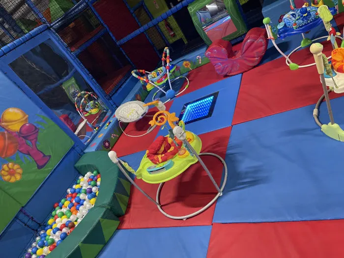 Overhead view of indoor play area with colourful soft play equipment, ball pits and climbing structures on padded flooring.