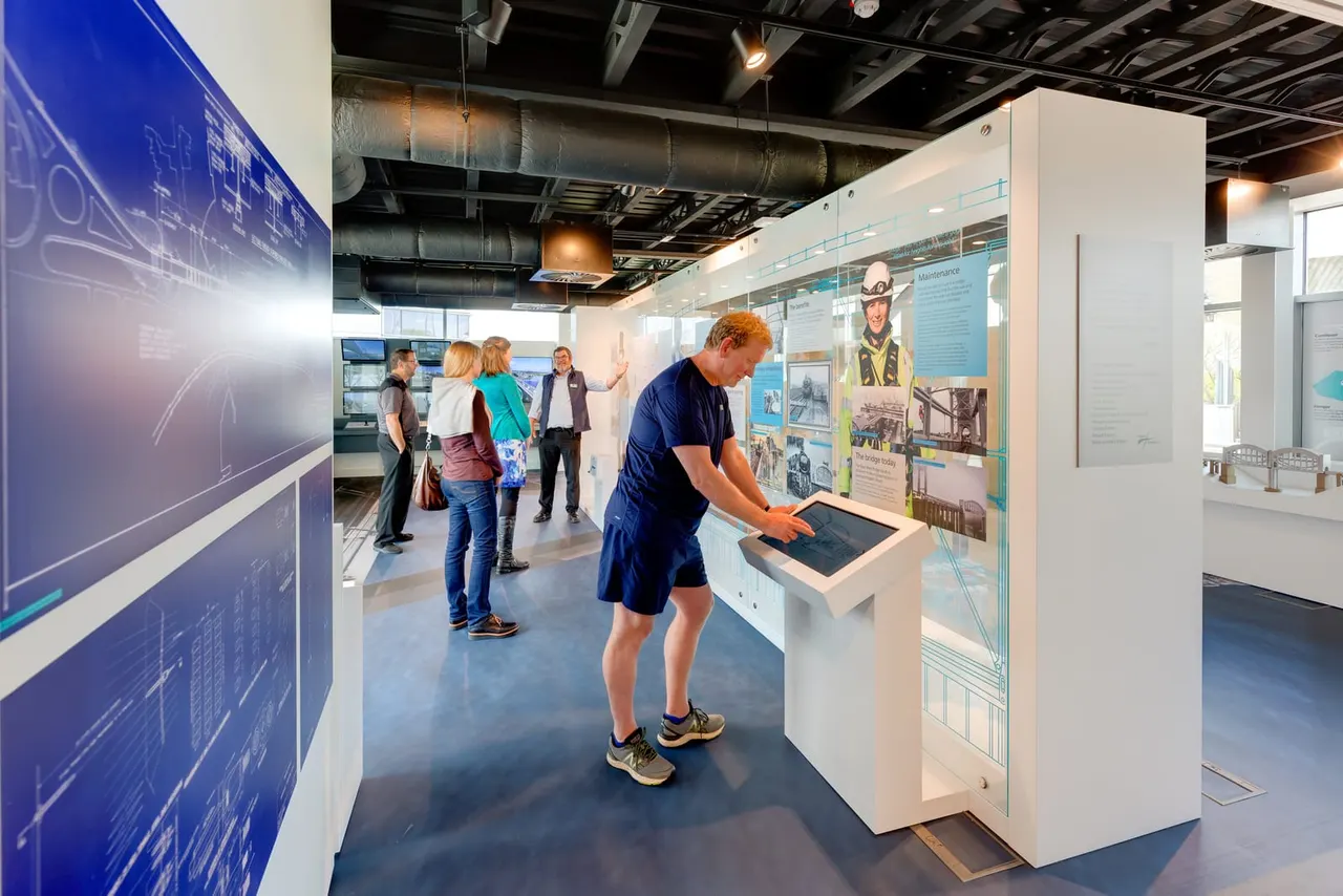 Visitors explore interactive displays and touch-screen exhibits in a modern museum gallery space.
