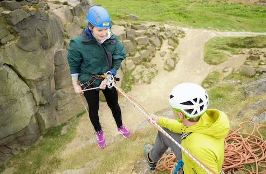Person abseiling down a rock face whilst another person manages the rope below.