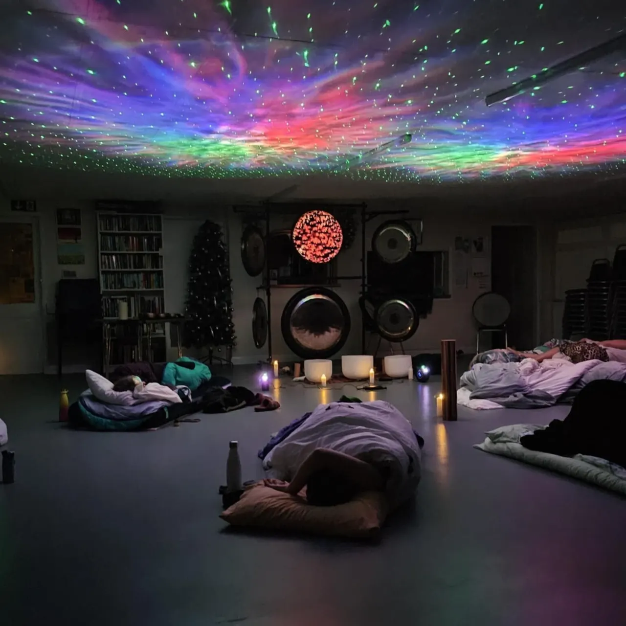 People lying on the floor in a darkened room with colourful galaxy projection on the ceiling and sound equipment on the walls.