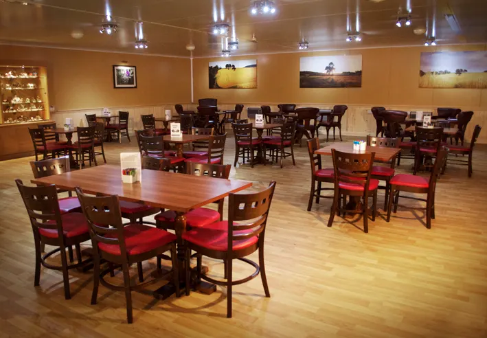 Spacious dining room with wooden tables, red-cushioned chairs, and landscape artwork on warm-toned walls.