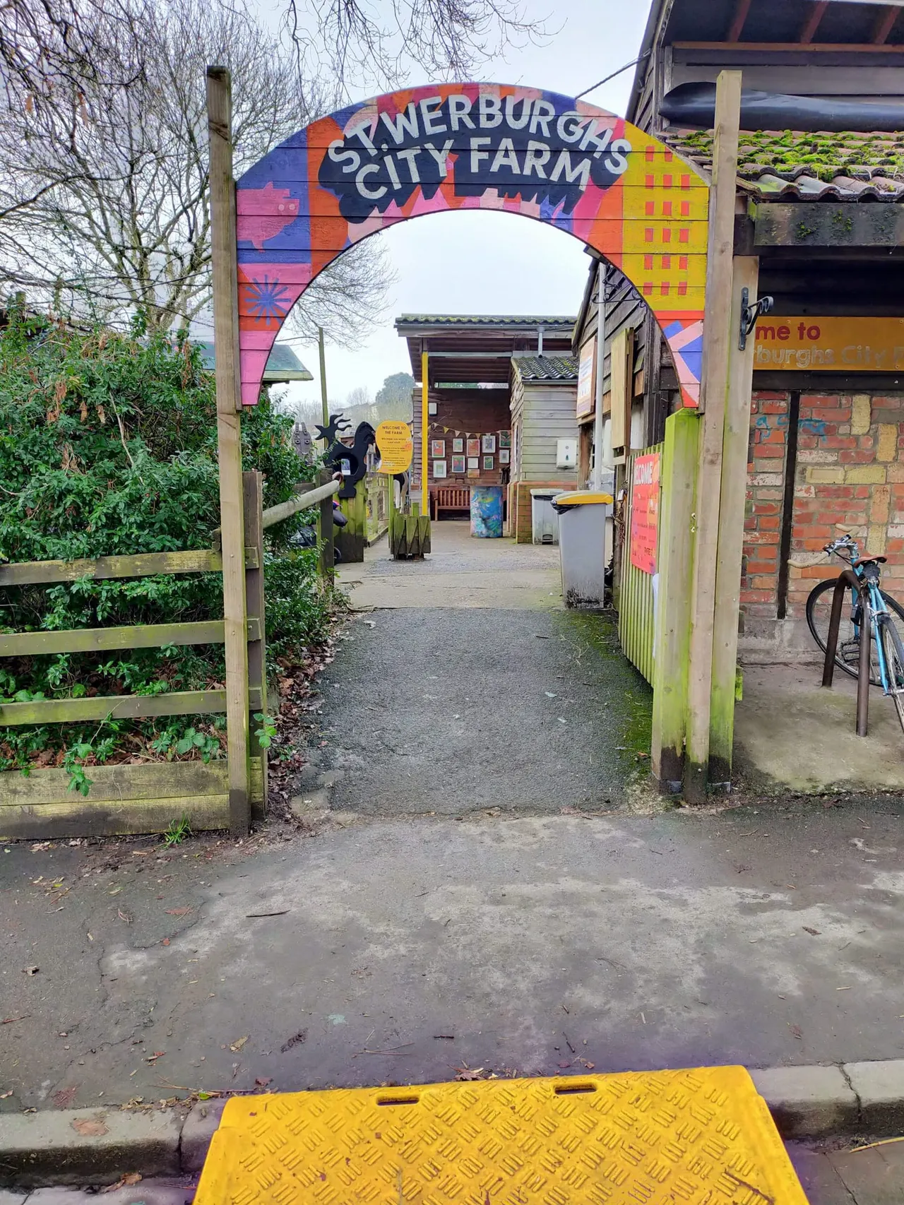 Colourful entrance arch to St Werburgh's City Farm with pathway, wooden gates, and farm buildings beyond.