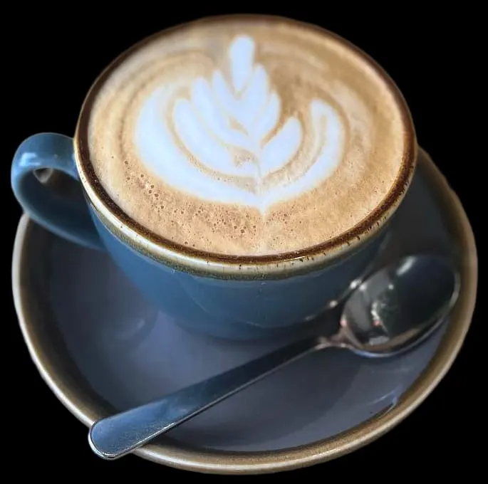 Blue cup of cappuccino with latte art leaf design on saucer with spoon.