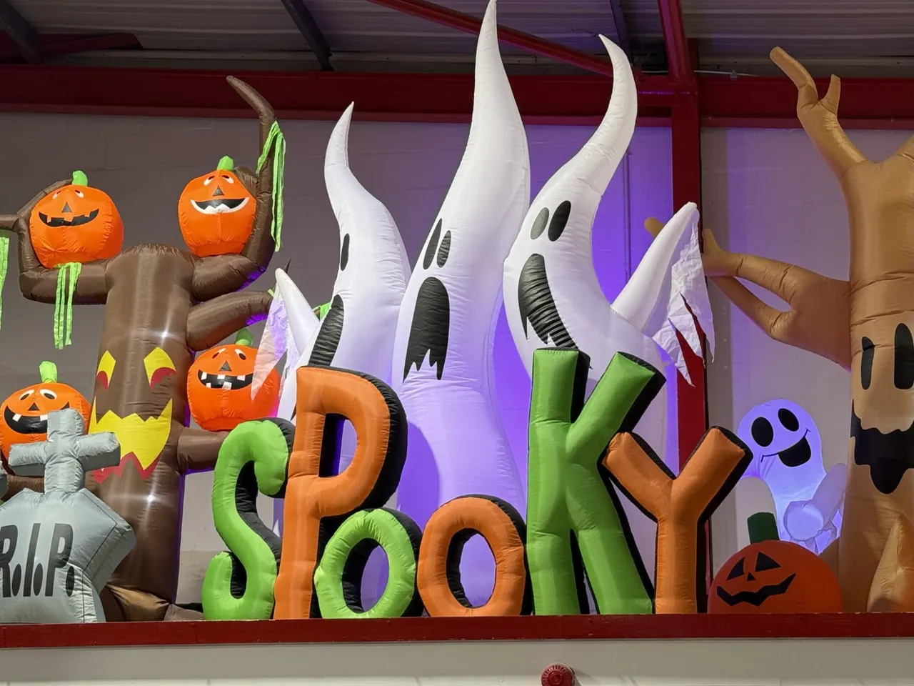 Inflatable Halloween decorations including ghosts, jack-o'-lanterns, skeletons and monsters displayed indoors under purple lighting.