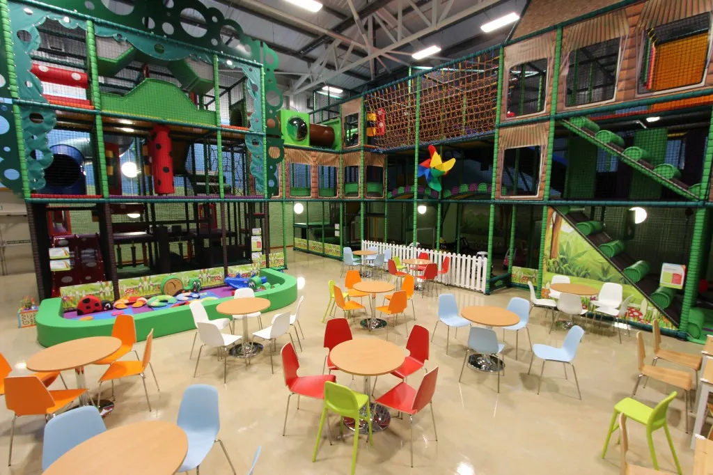 Colourful indoor soft play facility with multi-level climbing structures, seating areas and play equipment for children.