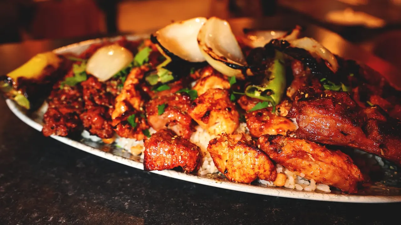 Grilled seafood and meat skewers with clams, garnished with fresh herbs on a white plate.