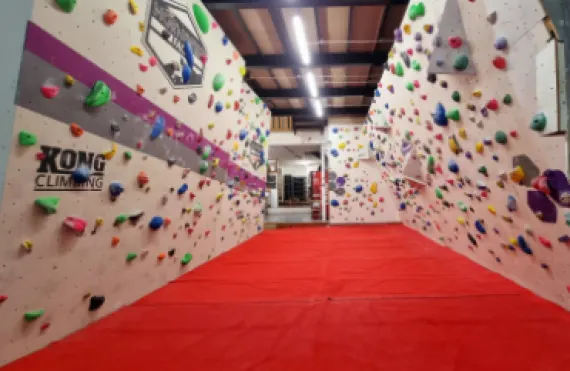 Interior of an indoor climbing wall facility with colourful handholds covering both walls and red matting on the floor.