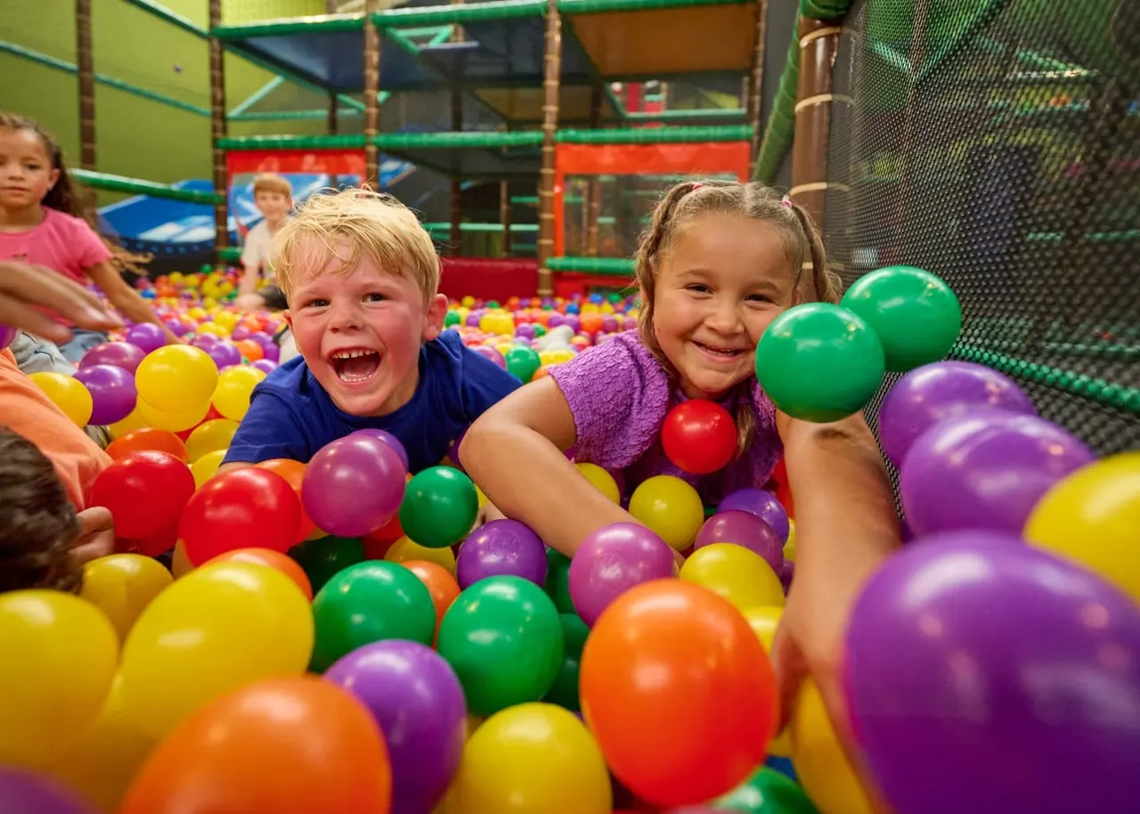 Children playing and laughing in a ball pit filled with multicoloured plastic balls in an indoor play centre.