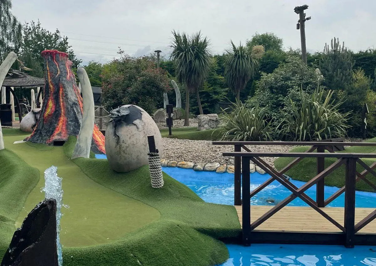 Outdoor mini golf course with themed volcanic and dinosaur-shaped obstacles on artificial green.
