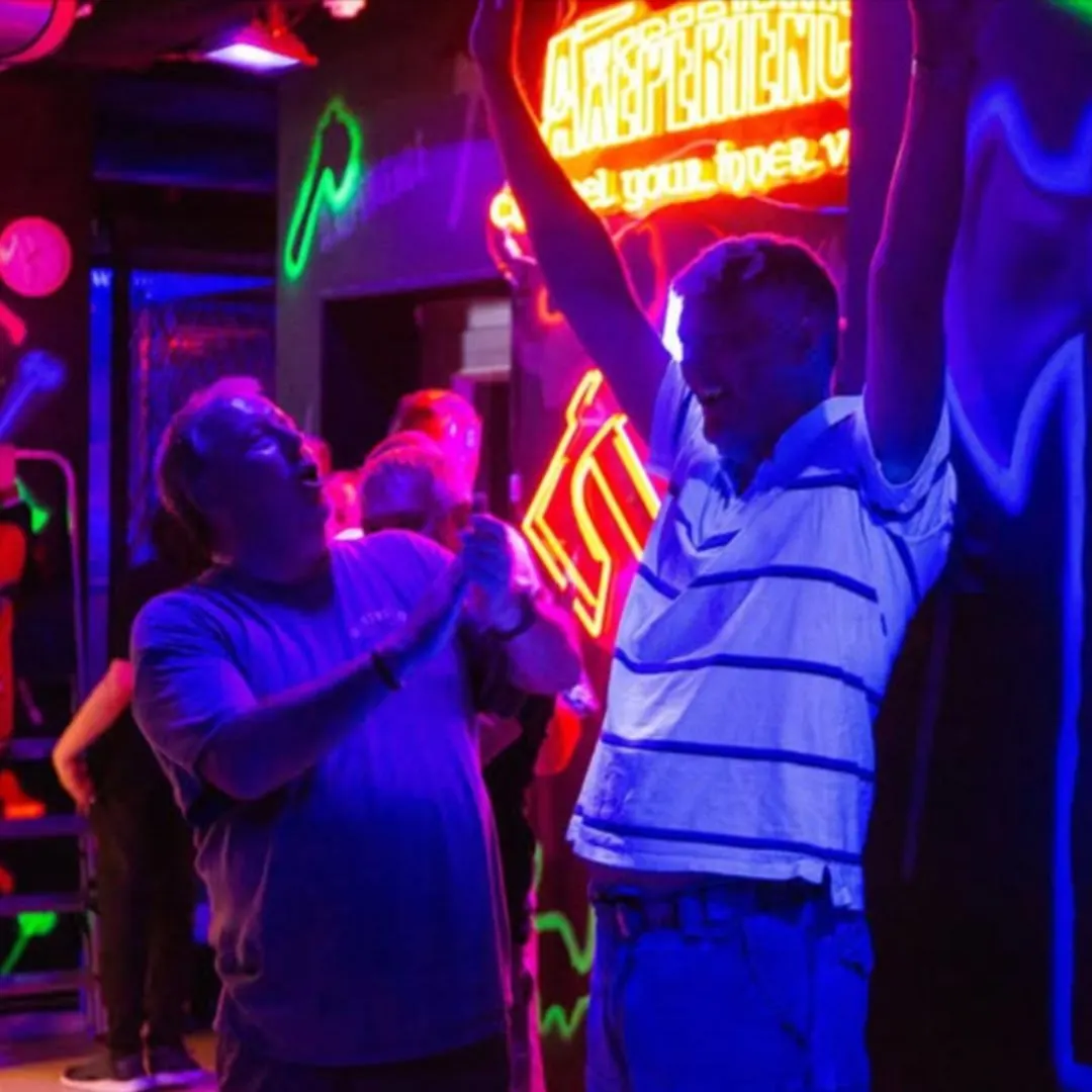 People enjoying axe throwing indoors under colourful neon lights at a venue.