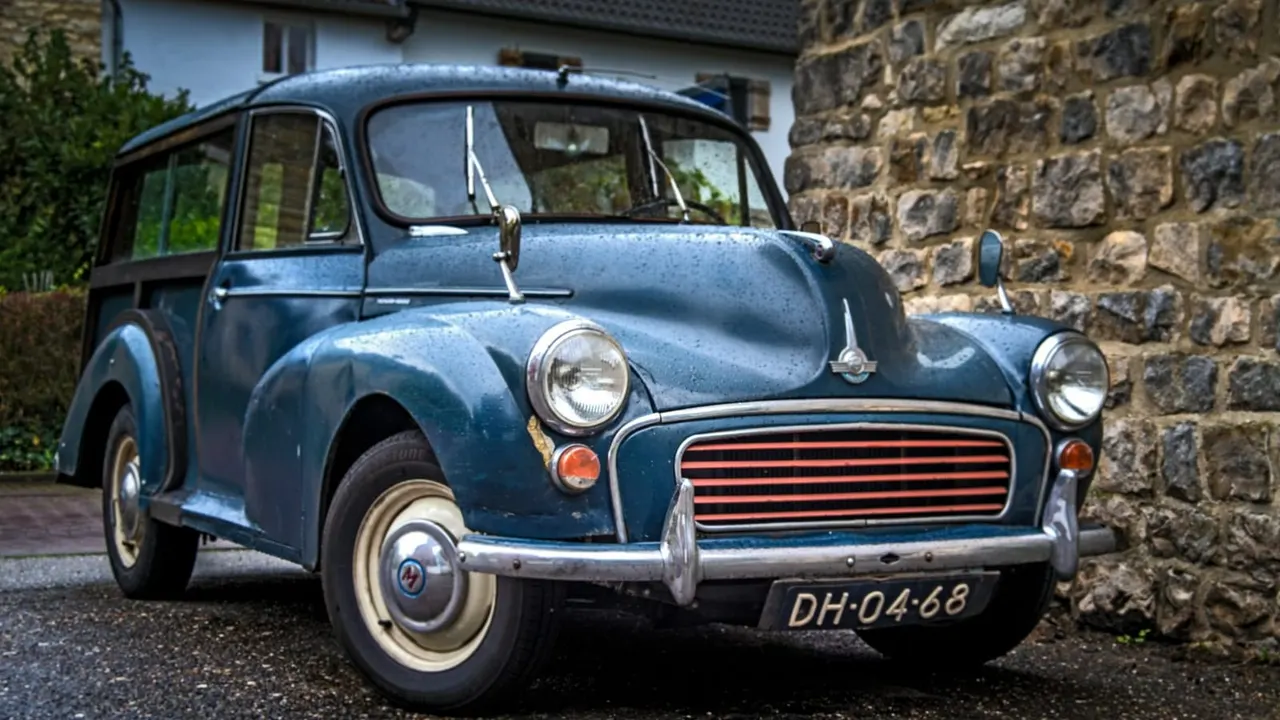 Blue vintage Morris Minor car parked beside a stone building.