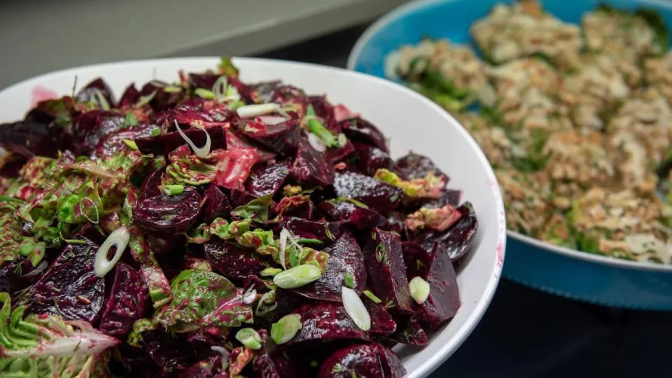 Beetroot salad with spring onions and herbs on a white plate, with a grain dish behind it.