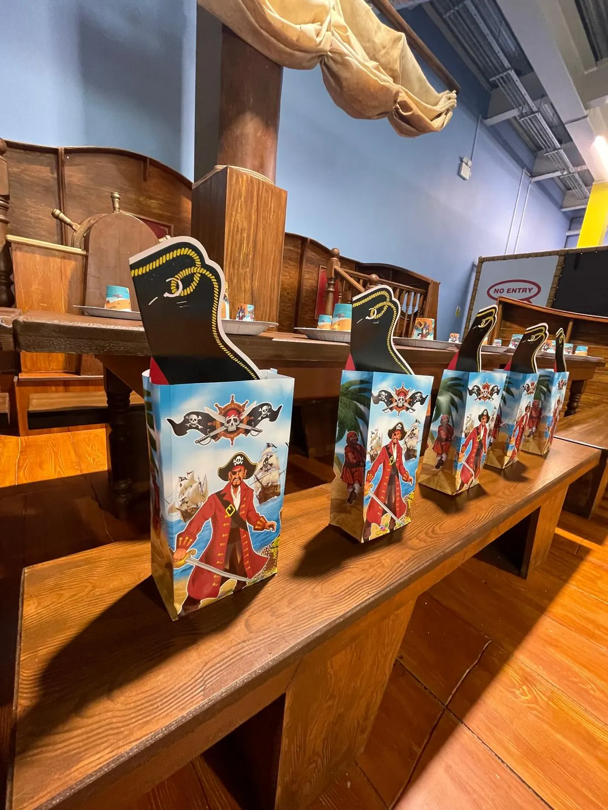 Pirate-themed cardboard cutout figures and decorative boxes displayed on wooden tables inside an indoor attraction.