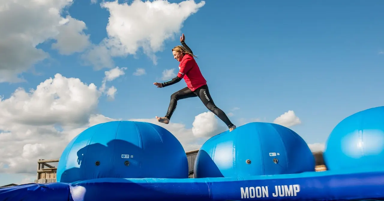 Person in red jacket jumping between blue inflatable domes on a bouncy obstacle course against blue sky.