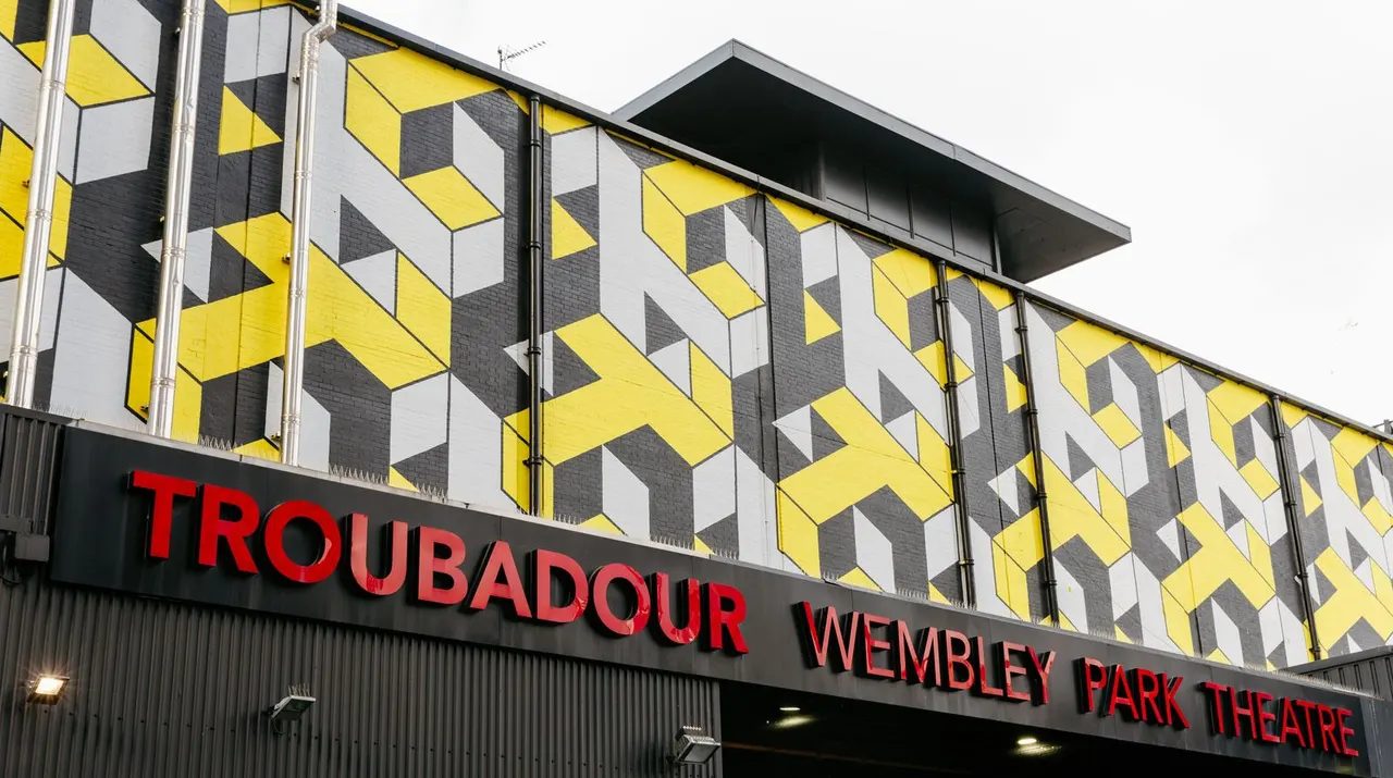 Modern theatre building with distinctive yellow, white and grey geometric facade and red illuminated signage.