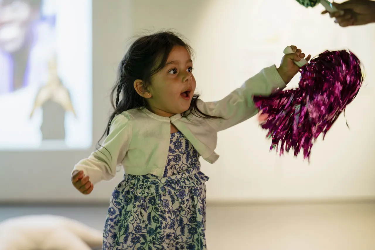 A young child holds up a vibrant purple fringed object with an expression of wonder and delight.