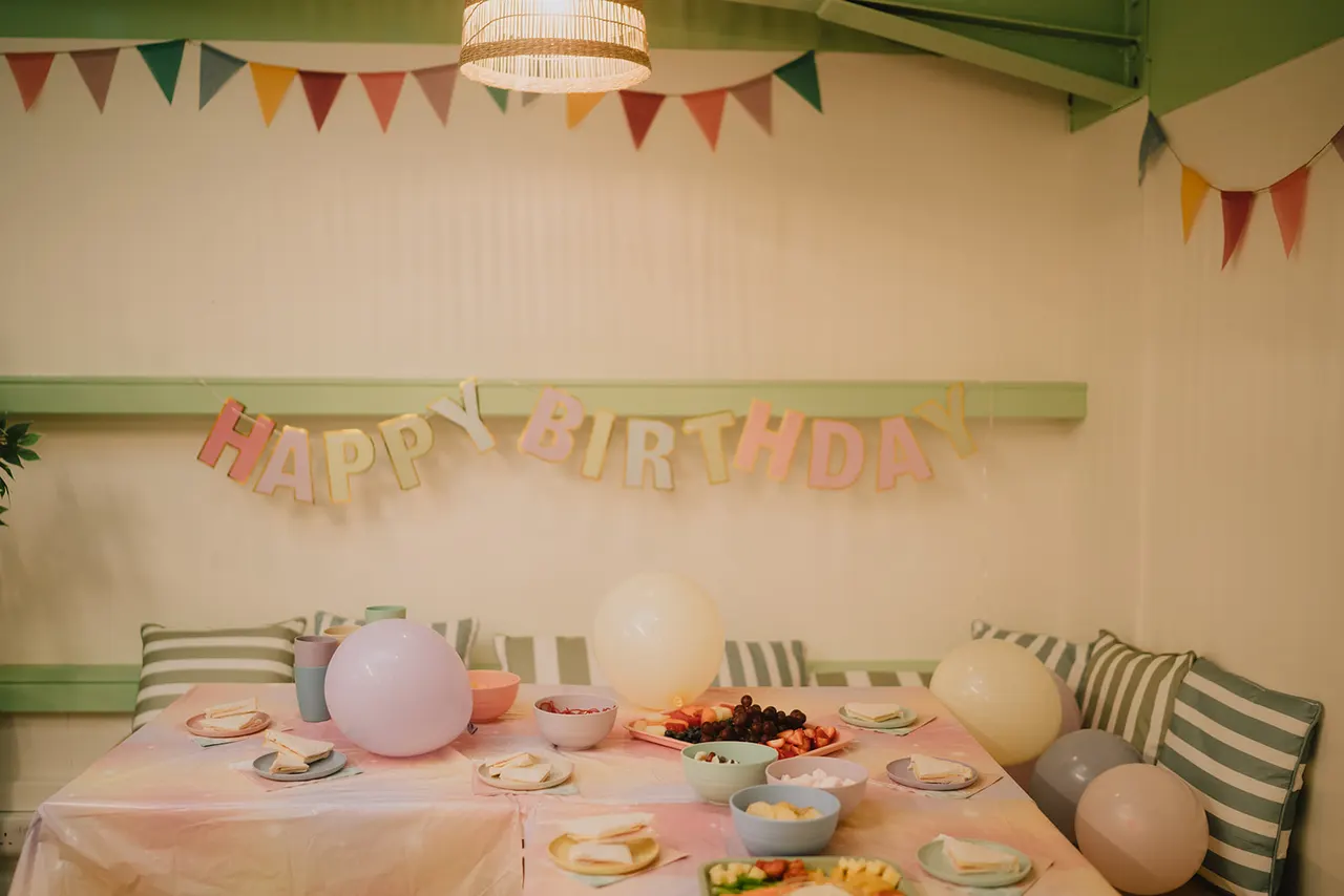A decorated party table set for a birthday celebration with balloons, bunting, plates, and food bowls.