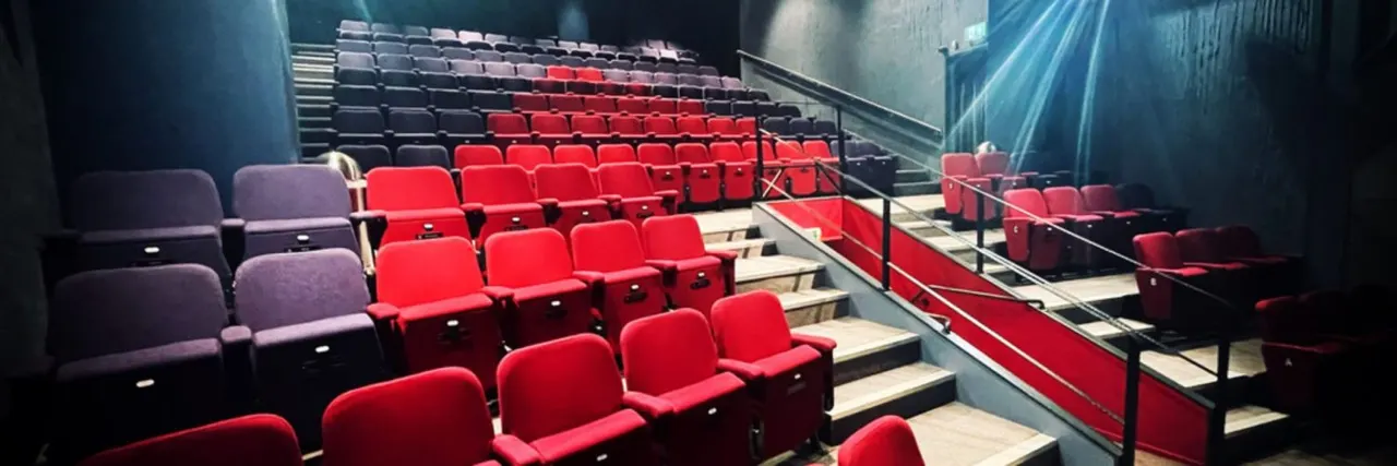 Empty cinema screen room with rows of red and purple seats arranged on tiered steps.
