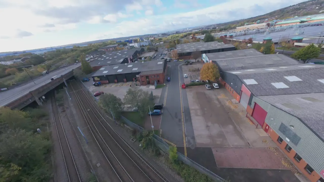 Aerial view of an industrial estate with railway tracks, warehouses, and parked vehicles in autumn daylight.