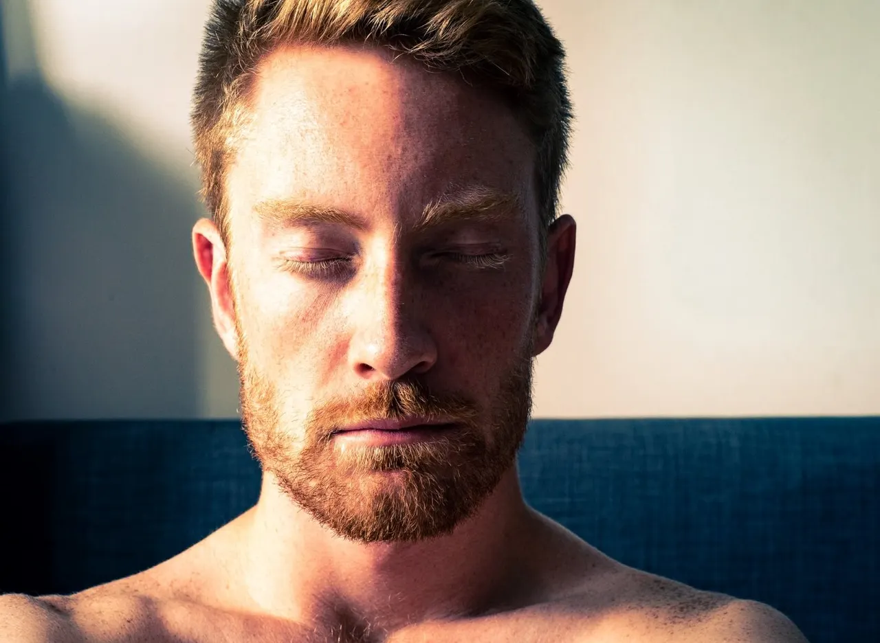Man with eyes closed in peaceful meditation pose outdoors by water.