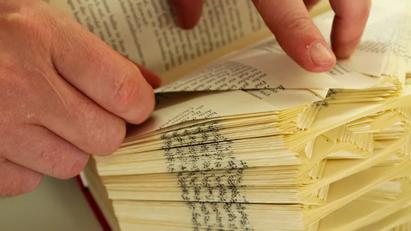 Hands holding open the pages of an old book with printed text visible on the aged paper.
