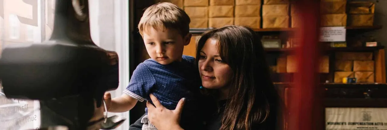 Woman holding a young child looking at a display in a museum with wooden cabinetry.