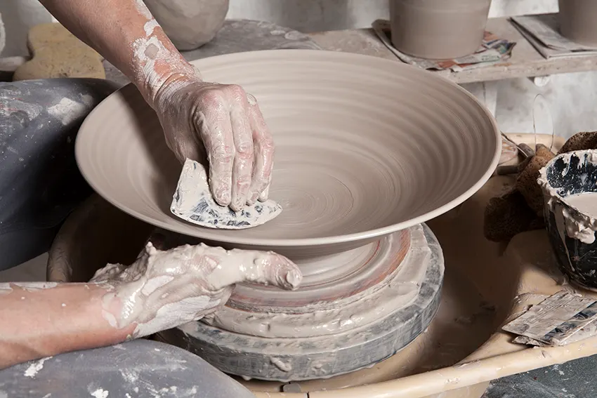 Two hands shaping clay on a pottery wheel, creating a vessel with spiral patterns.
