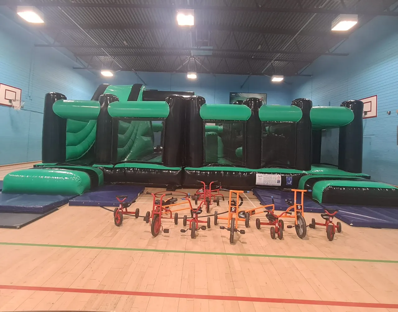 Sports hall set up for a children's bounce party with inflatable and trikes - same hall used for Friday roller disco