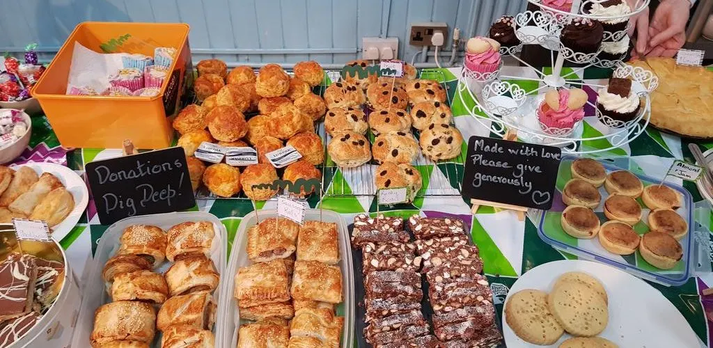 A bake sale display table with various homemade cakes, biscuits and pastries arranged on plates and trays.