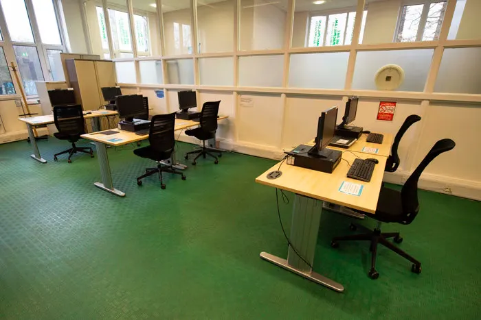 Modern office space with computer workstations, black chairs and desks on green flooring, bright windows.