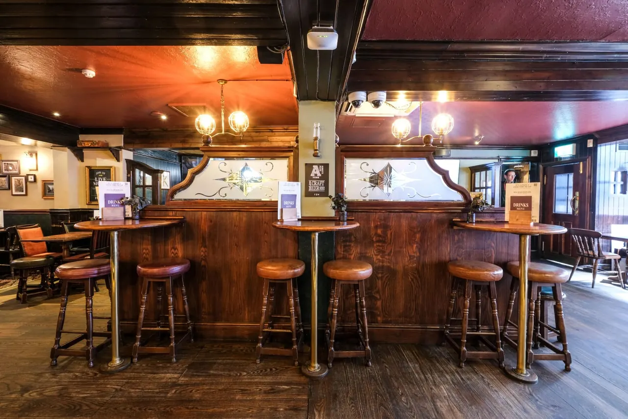 Empty bar interior with wooden counter, bar stools, pendant lighting and decorative mirrors above.