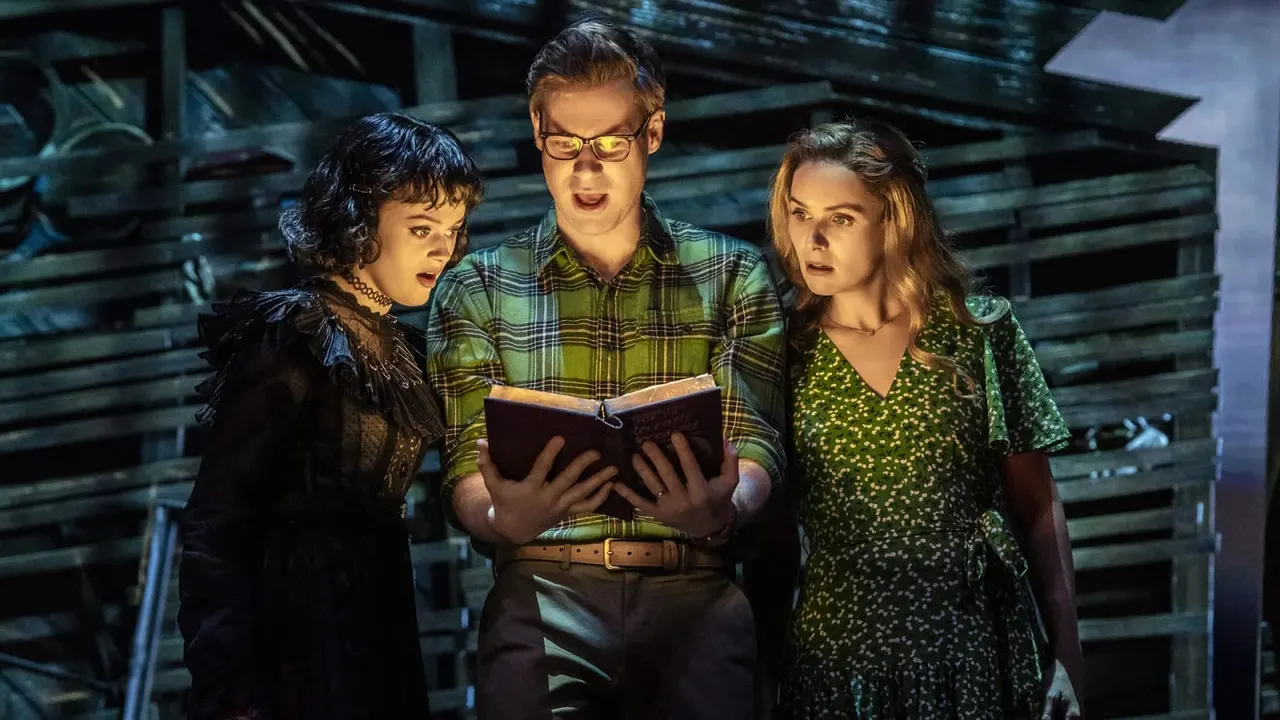 This is a photograph from a theatrical production showing three actors in period costume reading from a book together on stage.