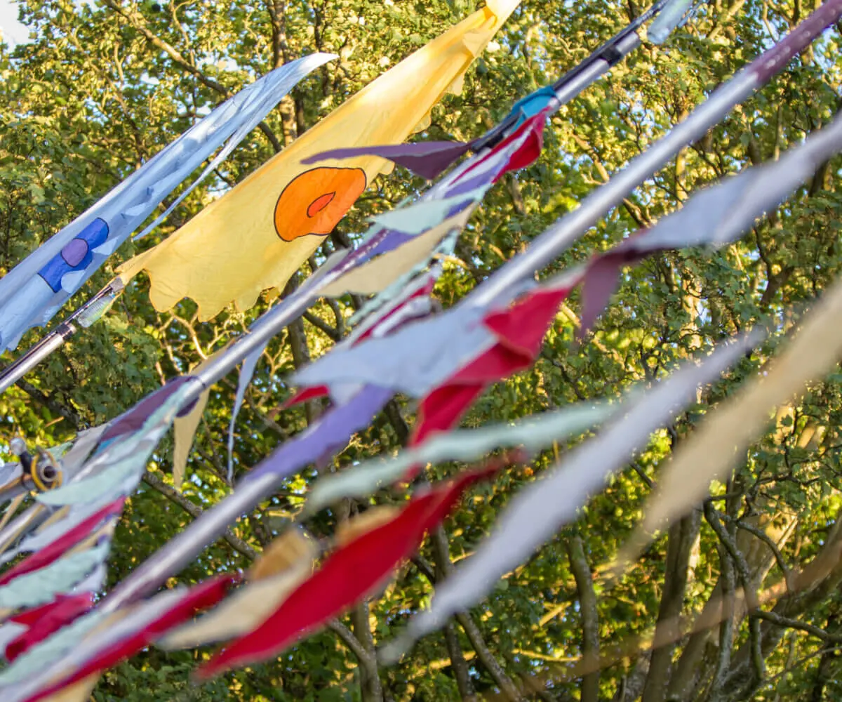 Colourful kites flying against green tree foliage on a sunny day.