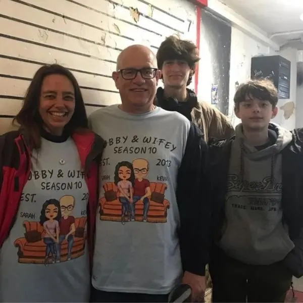 Four people standing indoors wearing casual clothing, two in matching "Abby & Wifey" themed t-shirts.